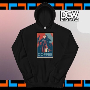 Op de afbeelding: Zwarte hoodie met een afbeelding van een personage met een mok en het woord "COFFEE" eronder. De afbeelding is rood, blauw en wit. De hoodie heeft een capuchon met trekkoord en een kangoeroezak.