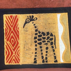 May include: A rectangular black fabric wall hanging with an African-inspired design. The central panel features a giraffe silhouette in black against a textured gold background. Red geometric patterns and white wavy lines frame the giraffe.