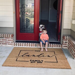 May include: A brown coir doormat with the text "The Landin Family Est. 2006" in black lettering. A young boy sits on the steps with a dog standing behind him.