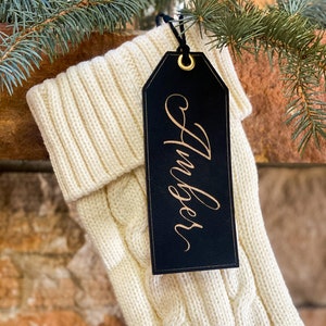 May include: A white knitted stocking with a black leather gift tag that says "Amber" in gold lettering.