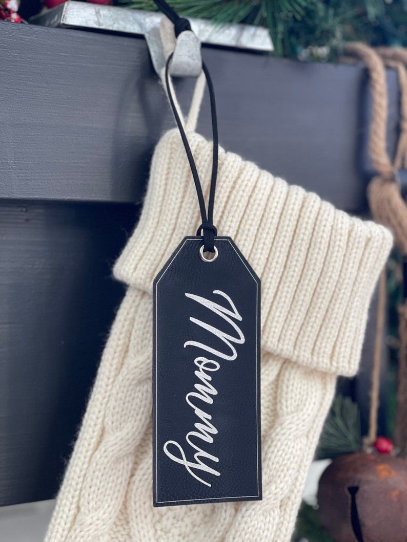May include: A black leather stocking tag with the word "Mommy" written in white script.