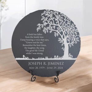 May include: A round dark gray slate memorial plaque featuring a white printed tree silhouette and the text: A limb has fallen from the family tree. I keep hearing a voice that says, Grieve not for me. Remember the best times, the laughter, the song. The good life I lived while I was strong. JOSEPH R. JIMENEZ MAY 28, 1979 - JUNE 29, 2024. It rests on a black metal stand.