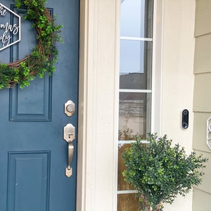 May include: A blue front door with a wreath and a silver door handle. A white sign with the text "The Thomas Family" is hanging on the door. A white sign with the text "No Soliciting" is hanging on the side of the house.