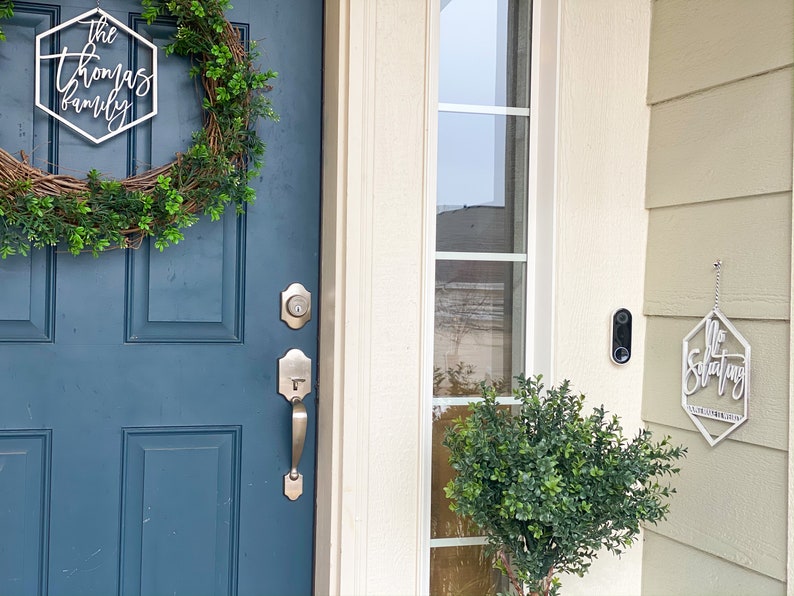 May include: A blue front door with a wreath and a silver door handle. A white sign with the text "The Thomas Family" is hanging on the door. A white sign with the text "No Soliciting" is hanging on the side of the house.