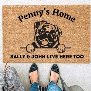 May include: A brown doormat with the text "Penny's Home" and a black silhouette of a pug dog peeking over the top. The text "Sally & John live here too" is printed below the dog.