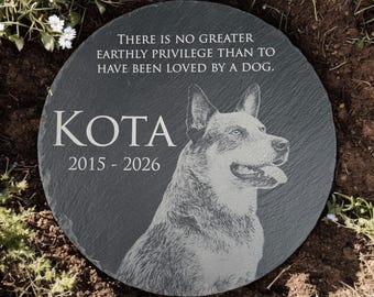 May include: A round dark gray slate memorial stone featuring an engraved portrait of a dog, the name KOTA, the years 2015-2026, and the text: There is no greater earthly privilege than to have been loved by a dog. The stone has a textured surface.