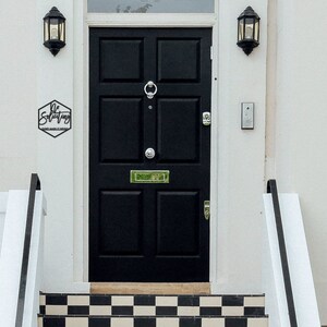 May include: A black front door with a hexagonal sign that reads "Be Solitary" above a black and white checkered tiled step.