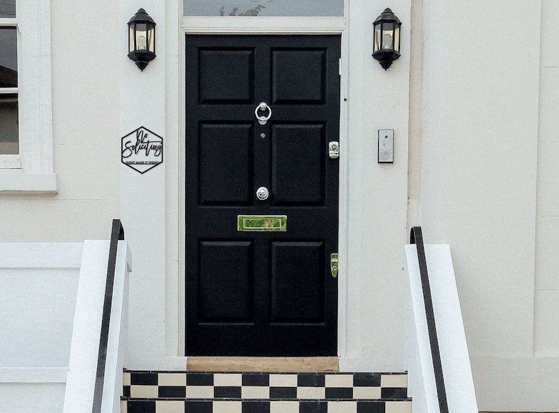 May include: A black front door with a hexagonal sign that reads "Be Solitary" above a black and white checkered tiled step.