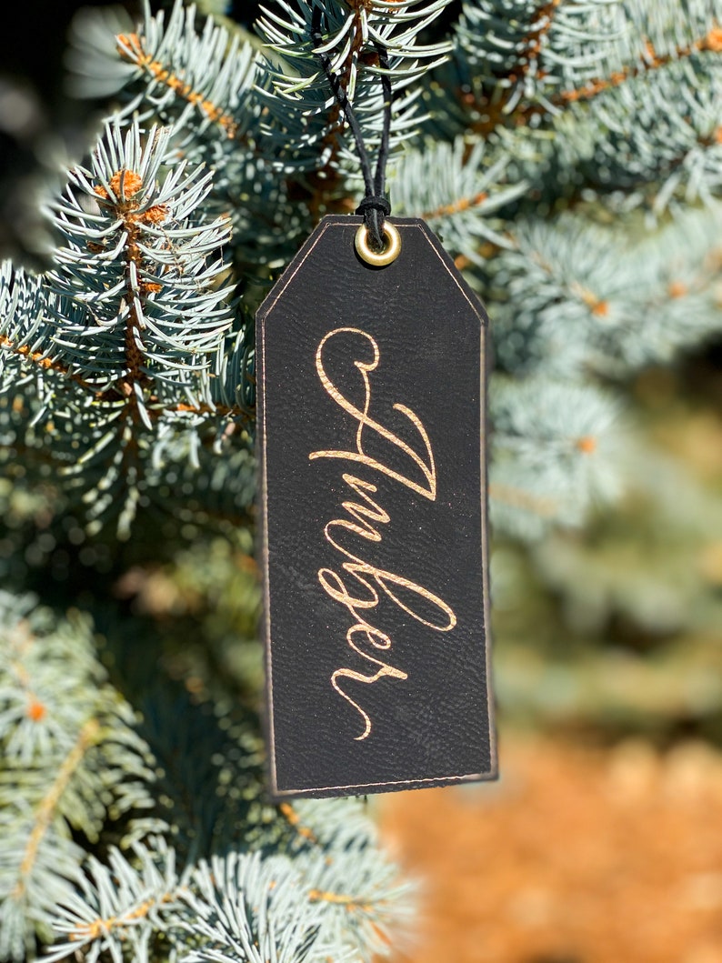 May include: Black leather gift tag with a gold inscription that reads "Huckleberry". The tag is hanging from a blue spruce tree.