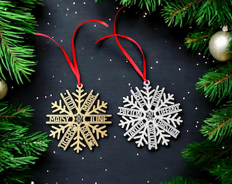 May include: Two snowflake-shaped ornaments with red ribbons. The gold ornament features the names Mark, June, Roo, Tiger, Maisy, and Judi with the year 2026. The silver ornament features the names Jonas, Tiffany, Christian, Payton, Taylor, Bella, and Payton with 2026.