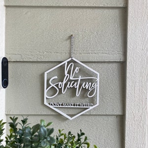 May include: White hexagon-shaped sign with the text "No Soliciting Don't Make It Weird" hanging on a light green wall.