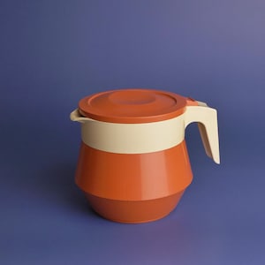 May include: A vintage orange and cream-colored pitcher with a matching lid and handle. The pitcher has a rounded base and a cylindrical body, with a cream-colored band around the middle. The handle is white.