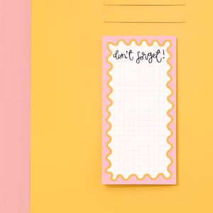 May include: A pink notepad with a yellow wavy border and the text "don't forget!" on the top. The notepad has a grid pattern and is on a yellow background.