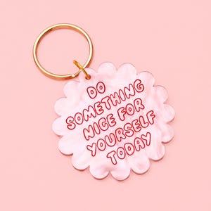 May include: A pink and white marbled keychain with a gold ring. The keychain is shaped like a flower and has the words "DO SOMETHING NICE FOR YOURSELF TODAY" in red lettering.