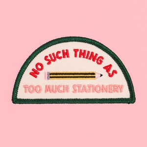 May include: A semi-circular embroidered patch with a dark green border and an off-white background. It features the red text NO SUCH THING AS, a yellow and black striped pencil graphic, and the pink text TOO MUCH STATIONERY.