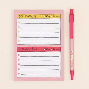 May include: Pink notepad with two sections for "top priorities" and "if there's time". Each section has a checklist with lines for writing and a checkbox for "today" and "this week". A pink pen with the words "work in progress" is next to the notepad.