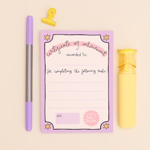 May include: A lilac certificate of achievement with a pink interior, featuring the text "certificate of achievement" and lines for writing. A purple marker, yellow highlighter, and yellow paper clip are also present.