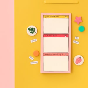 May include: A pink to-do list notepad with three sections labelled "bare minimum", "if there's time", and "absolutely smashing it". Each section has a blank space for writing and a small red circle for marking tasks as done. The notepad is on a yellow surface with various colourful stickers and small paper notes.