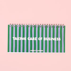 May include: A horizontal weekly planner with a spiral binding at the top. The cover features vertical stripes in alternating shades of green and light purple. The text TAKING CARE OF BUSINESS is printed in white, with WEEKLY PLANNER below it.