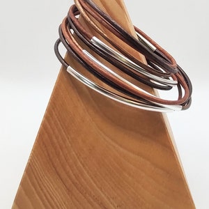 May include: A stack of brown leather bracelets with silver accents displayed on a wooden stand.