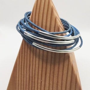 May include: A stack of blue leather bracelets with silver metal accents. The bracelets are displayed on a wooden stand.