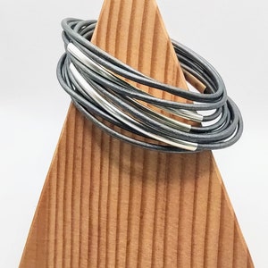 May include: A stack of silver and gray leather bracelets on a wooden display stand.