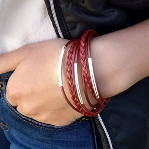 May include: A red braided leather bracelet with silver accents. The bracelet is worn on a person's wrist.
