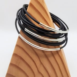 May include: A stack of black leather bracelets with silver metal accents. The bracelets are displayed on a wooden stand.