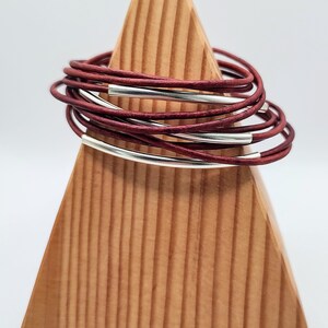May include: A stack of maroon leather bracelets with two silver metal bands.