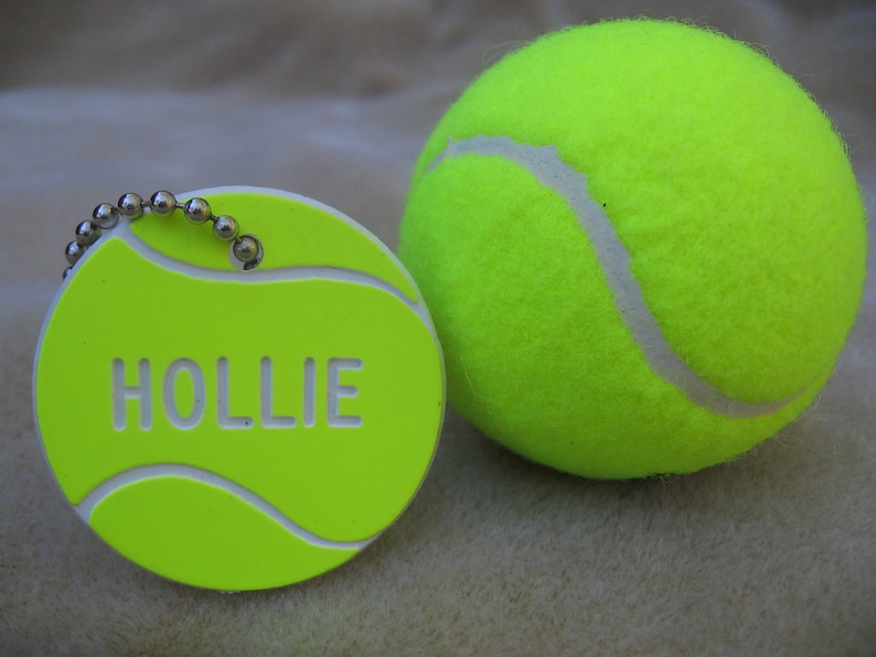 May include: A bright green tennis ball and a matching round keychain. The keychain has the name "HOLLIE" in white letters. The keychain has a silver ball chain attached.
