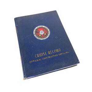 May include: A vintage navy blue "Cruise Record" book from the 95th Naval Construction Battalion. The cover features a circular emblem with text and a red and gold design. The book's title is in gold lettering.