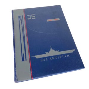 May include: A navy blue book with the text "36" and "1951-1953" in the upper right corner. The book features a silver illustration of a ship and the text "USS ANTIETAM". A gray and red vertical design is on the left side.