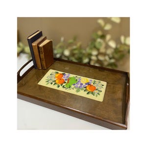 May include: A wooden serving tray with a rectangular embroidered runner featuring a design of oranges, lemons, grapes, and flowers. The runner is cream colored with green, orange, yellow, and purple accents.