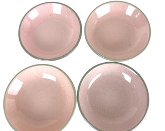May include: A set of four round bowls featuring a soft pink base color with a subtle speckled pattern throughout the interior and exterior surfaces. Each bowl has a smooth, rounded rim and a consistent, shallow depth, presented from a top-down view.