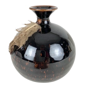 May include: A black ceramic vase with a brown glaze and a feather accent. The vase has a round body and a narrow neck.