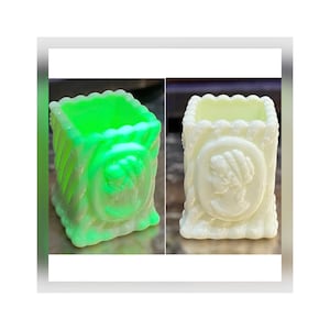 May include: Two small, rectangular glass vases. One is a bright, neon green, and the other is a creamy white. Both feature a cameo design and a textured, ribbed exterior. The vases have a scalloped top edge.