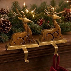 May include: Two gold-toned metal stocking holders, each featuring a stylized deer figure with an openwork cutout design on the body. The deer are mounted on rectangular bases with integrated hooks extending downward for hanging stockings.