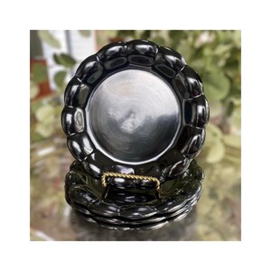 May include: A stack of four black ceramic plates with a scalloped edge design. The plates are displayed on a gold-colored metal stand. The plates have a glossy finish and a reflective surface.