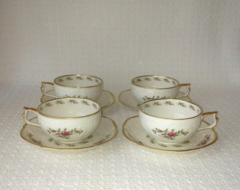 May include: Set of four white teacups and saucers with a floral pattern and gold trim. The cups and saucers have a delicate, embossed design.