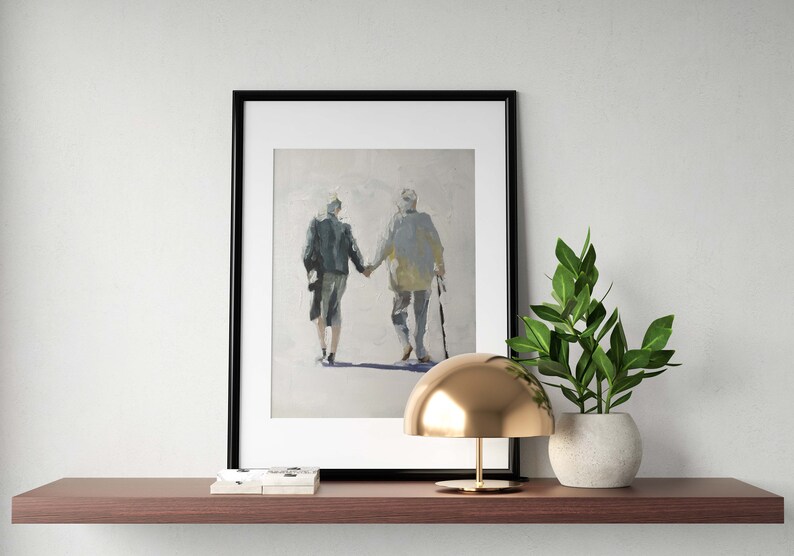 May include: Framed art print depicting two figures holding hands, walking away. The painting features muted tones of gray, blue, and yellow. The artwork is displayed on a dark brown shelf, alongside a gold lamp and a potted plant.