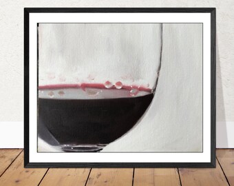 May include: A framed print of a wine glass filled with dark red wine. The glass is partially visible, with the wine occupying the lower portion. Small droplets cling to the glass near the wine's surface, against a white background.