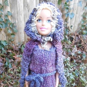May include: A doll wearing a purple and blue knitted hooded dress with a white and brown fur trim. The doll has blonde hair and blue eyes.