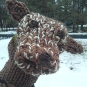 May include: A brown and white knitted puppet in the shape of a deer's head. The puppet is in focus and the background is blurred.