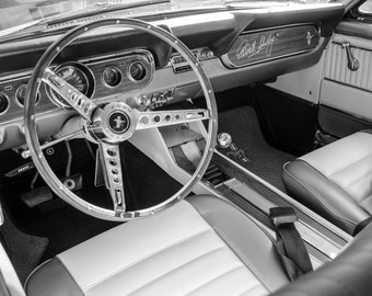 Pode incluir: Fotografia a preto e branco do interior de um carro clássico. O volante tem uma borda de madeira e um design de raios prateados. O painel tem um acabamento de madeira e uma assinatura que diz "Carroll Shelby".