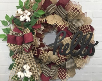 May include: A burgundy and brown checked wreath with a burlap bow, cotton sprigs, and a black wooden sign that says "hello".