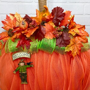 May include: Orange tulle pumpkin wreath decorated with autumn leaves, berries, and a welcome sign.