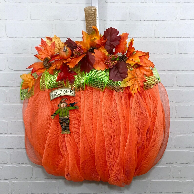 May include: Orange mesh pumpkin wreath decorated with autumn foliage, a scarecrow, and a sign that reads "Welcome".