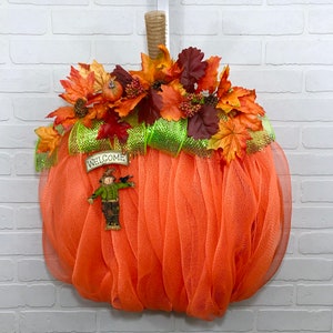 May include: Orange mesh pumpkin wreath decorated with autumn leaves, a scarecrow, and a welcome sign.