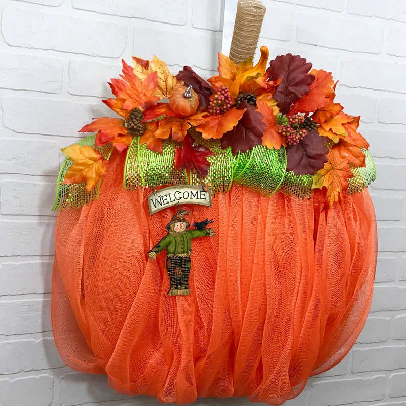 May include: Orange mesh pumpkin wreath decorated with autumn leaves, a scarecrow, and a welcome sign.