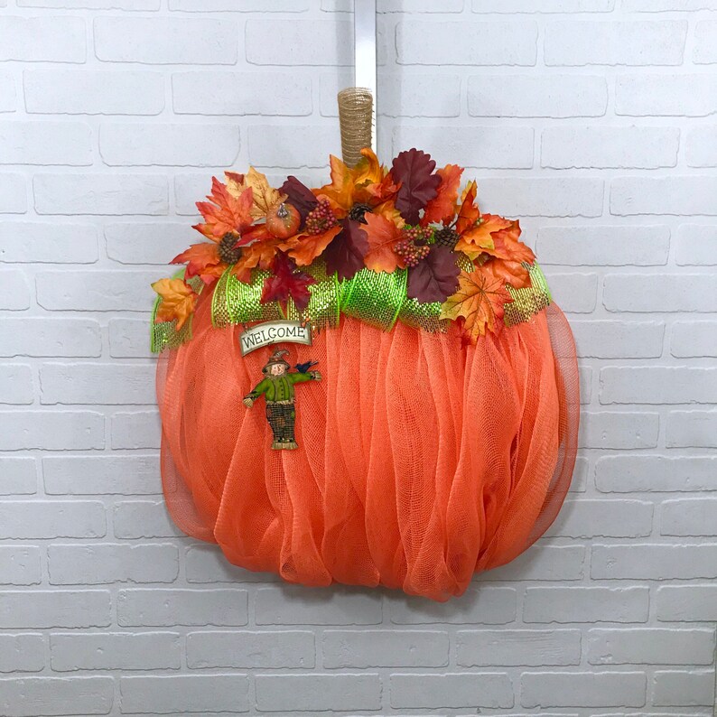 May include: Orange mesh pumpkin wreath decorated with autumn leaves, a scarecrow, and a sign that reads "Welcome".